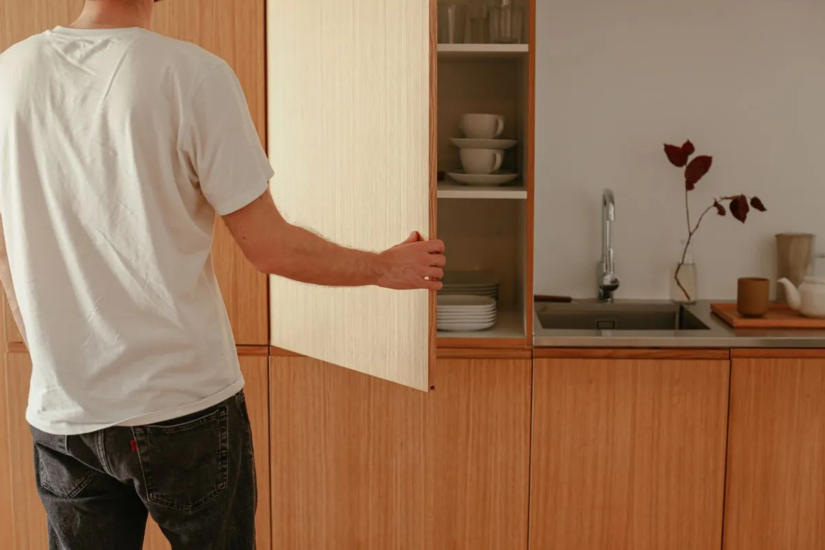 A person opening a tall oak cabinet door